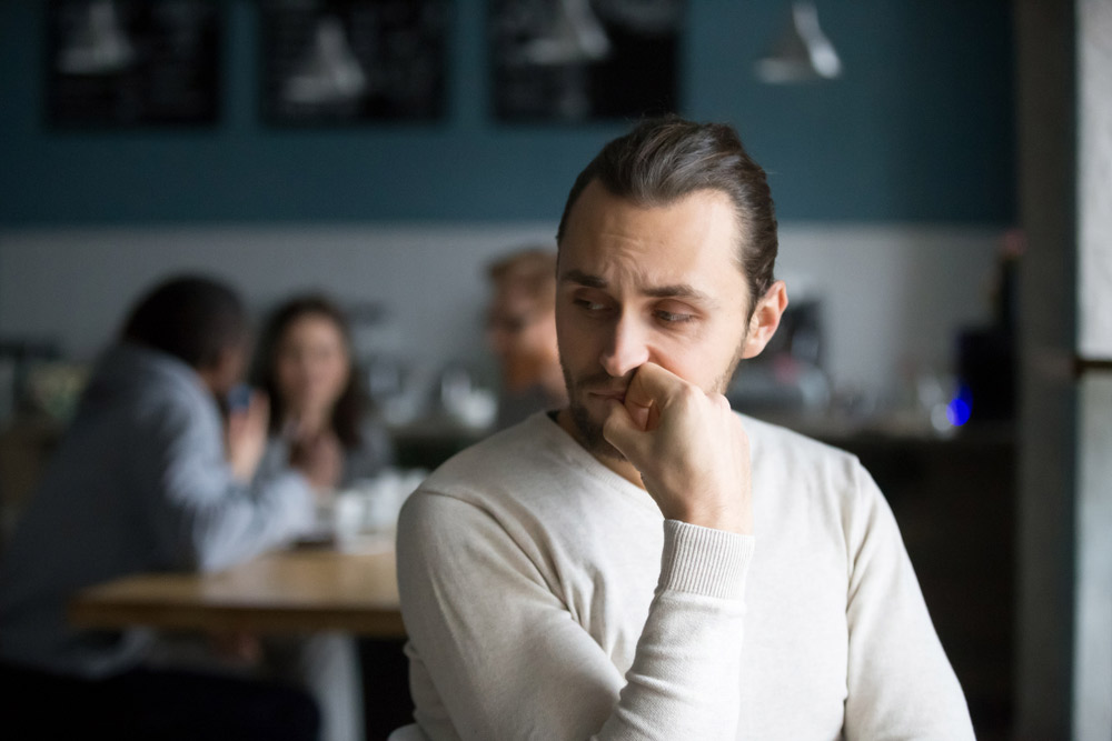worried looking young man with muted image of people in the background