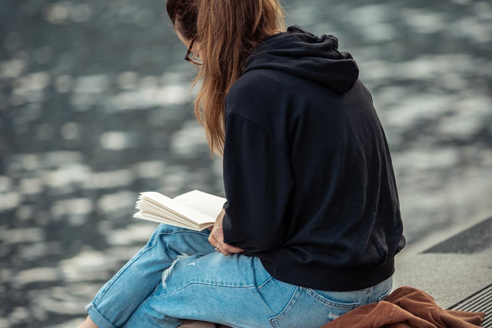 a woman wearing black sweater reading a book in a lake port 