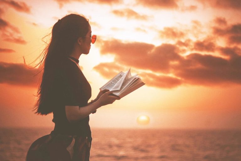 photo of a woman reading a memoir on the beach during sunset