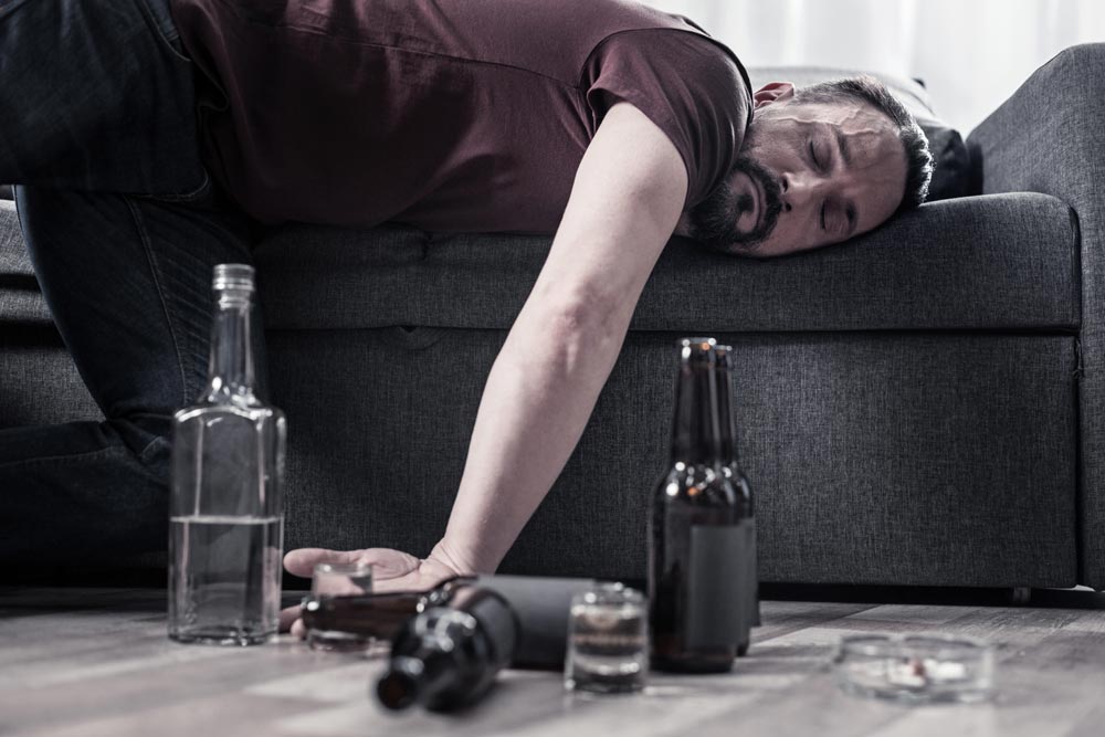 Drunk bearded adult man lying on the sofa and sleeping after drinking lots of alcohol
