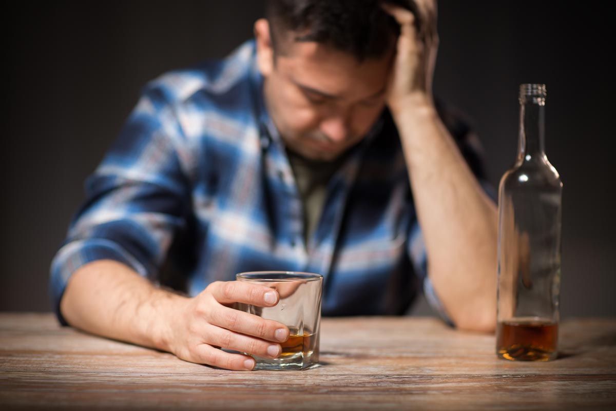 male alcoholic with bottle and glass drinking whiskey at night