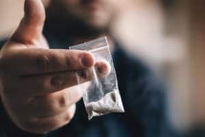 Drug dealer offers cocaine dose or another drugs in plastic bag, drug addiction on party concept, selective focus, toned