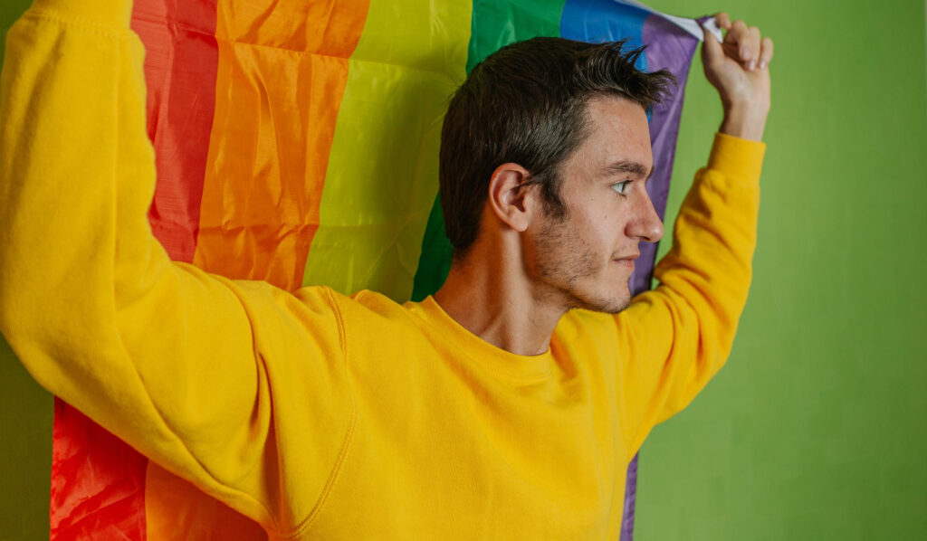 A young man suffering from mental health issues holding the LGBTQ flag up.